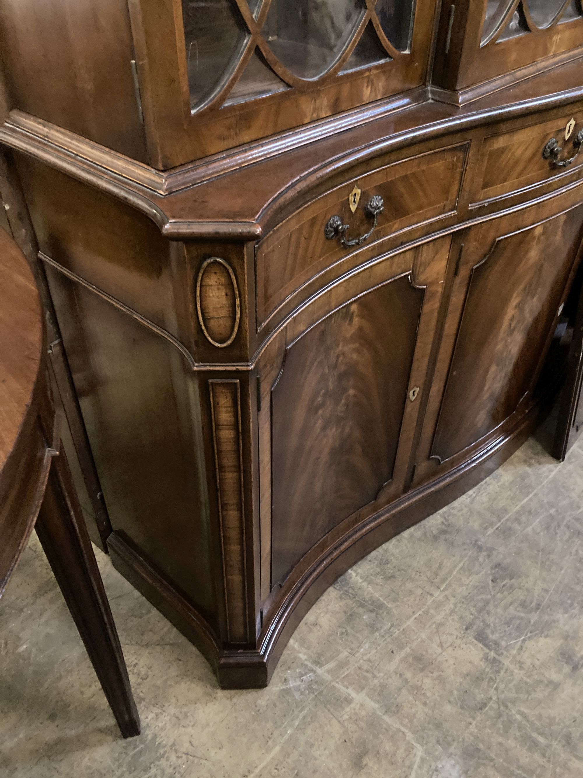 A George III style mahogany and walnut banded breakfront bookcase, with pierced broken swan neck pediment over oval glazing bars,